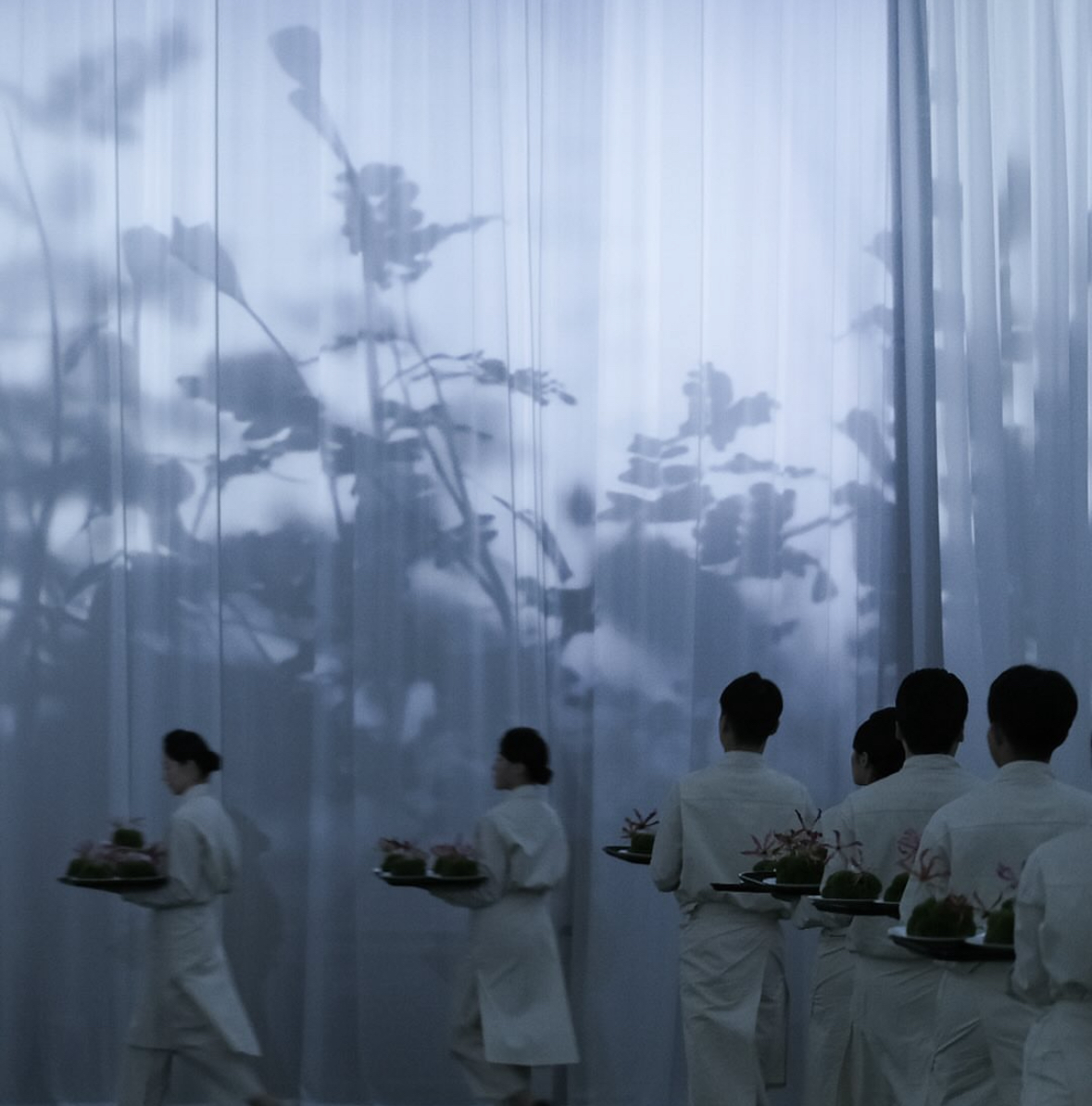 Servers carrying plated dishes in a line at a Secret Supper 404 event